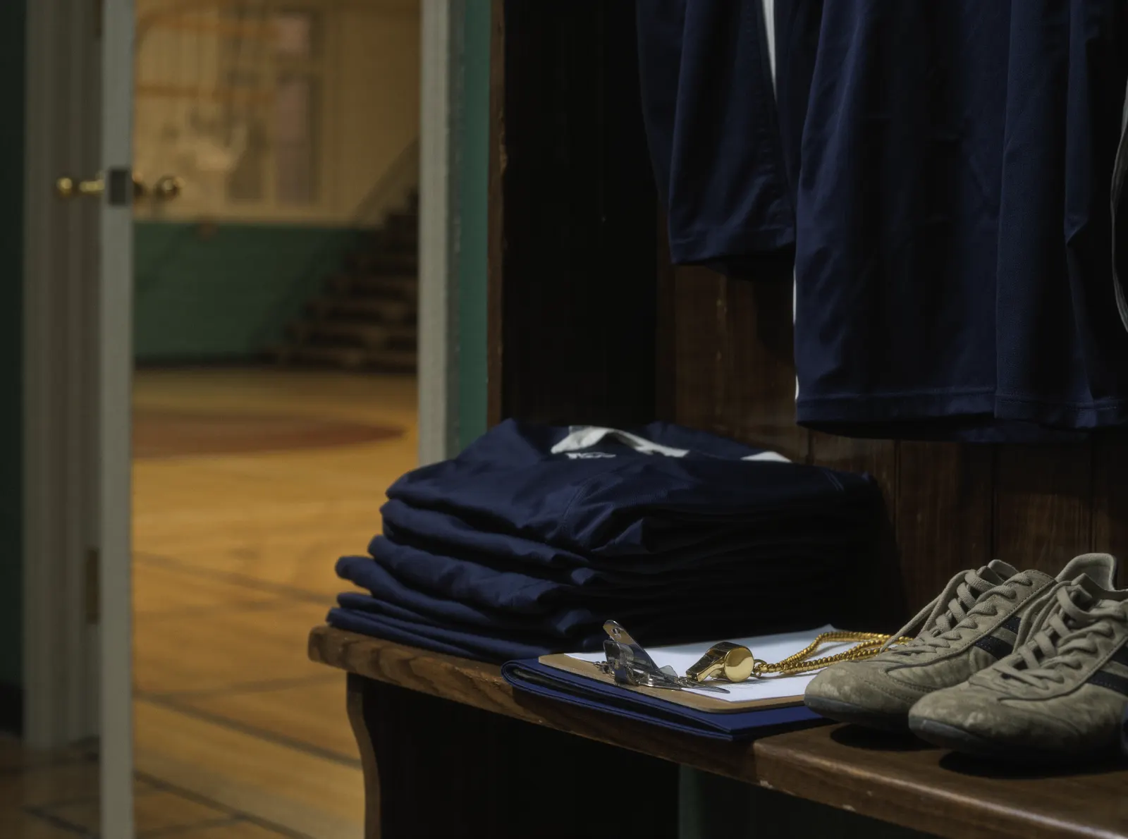 Des maillots de club pliés sur un banc, un sifflet et des chaussures de sport, la salle en arrière-plan.